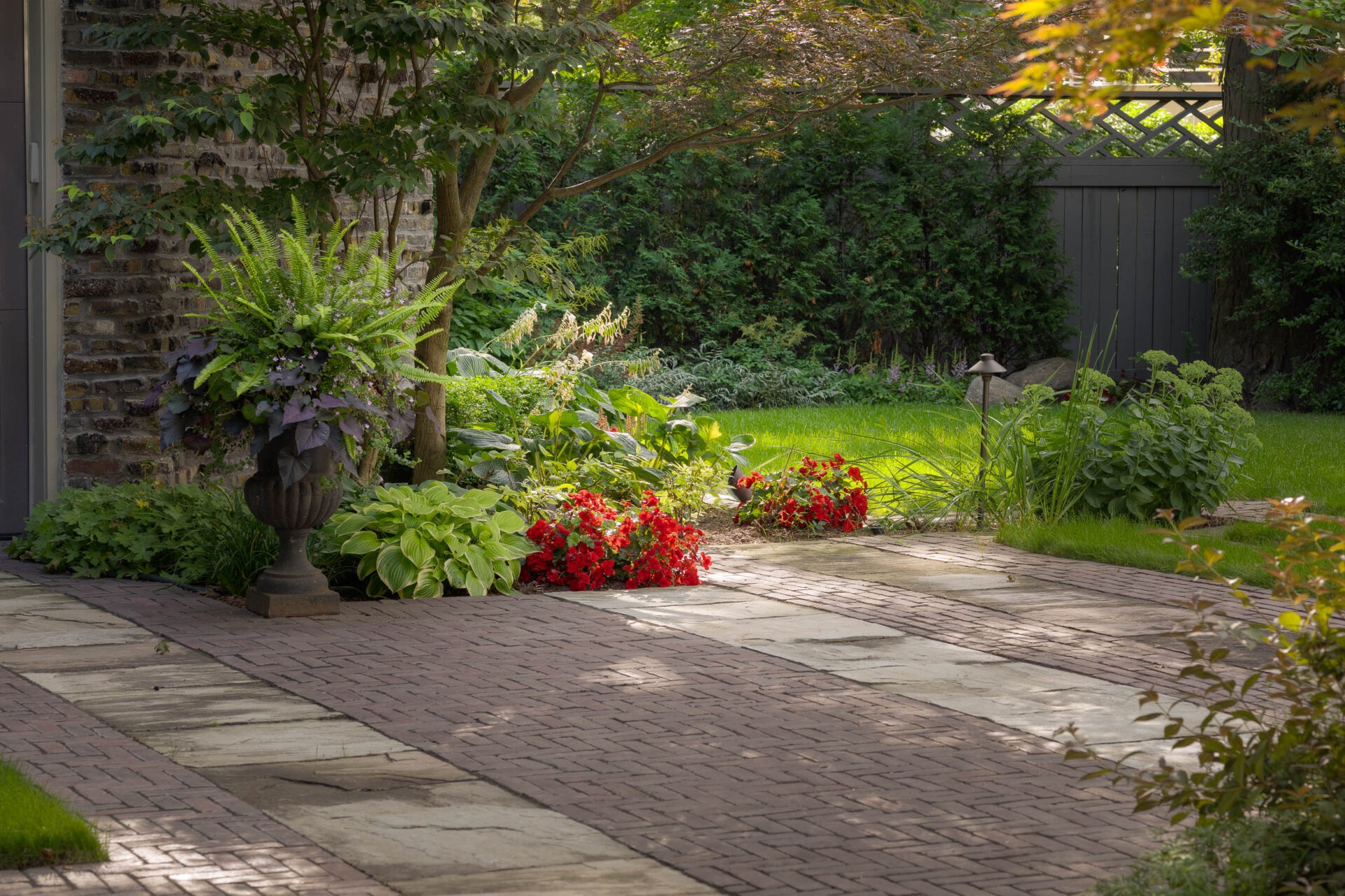 A serene garden with vibrant flowers, lush greenery, and stone path next to a brick building, providing a peaceful outdoor setting.