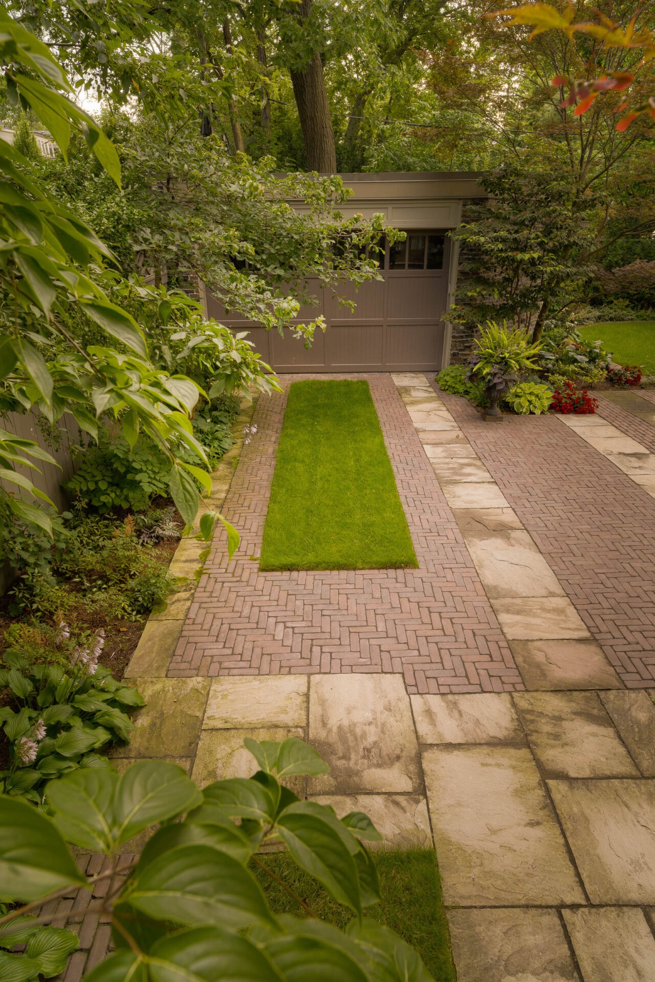 A peaceful garden with lush greenery, brick pathways, and a wooden shed; surrounded by trees and ornamental plants in a serene setting.