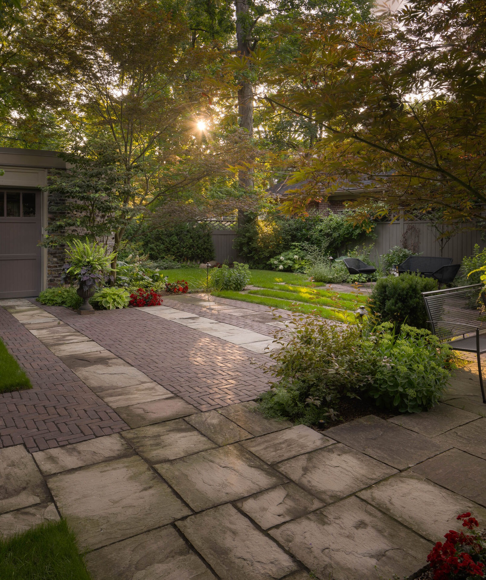 A serene garden with stone paths, lush greenery, and blooming flowers. Sunlight filters through trees, casting a warm, inviting glow.