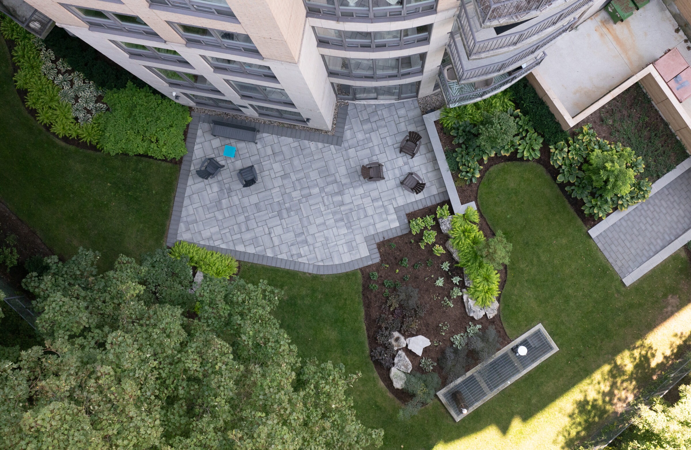 Aerial view of a landscaped patio area with seating, surrounded by greenery next to a modern building with multiple windows.