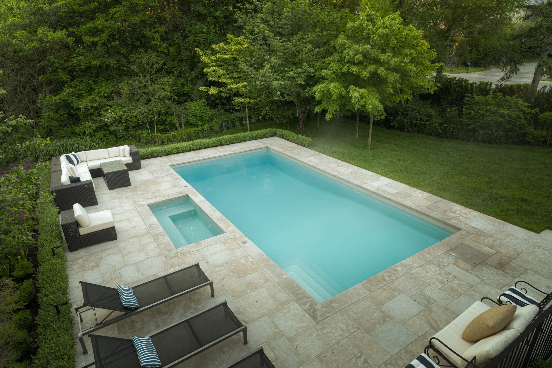 A serene backyard with a rectangular pool, surrounded by greenery, patio furniture, and sun loungers. Peaceful and inviting atmosphere.