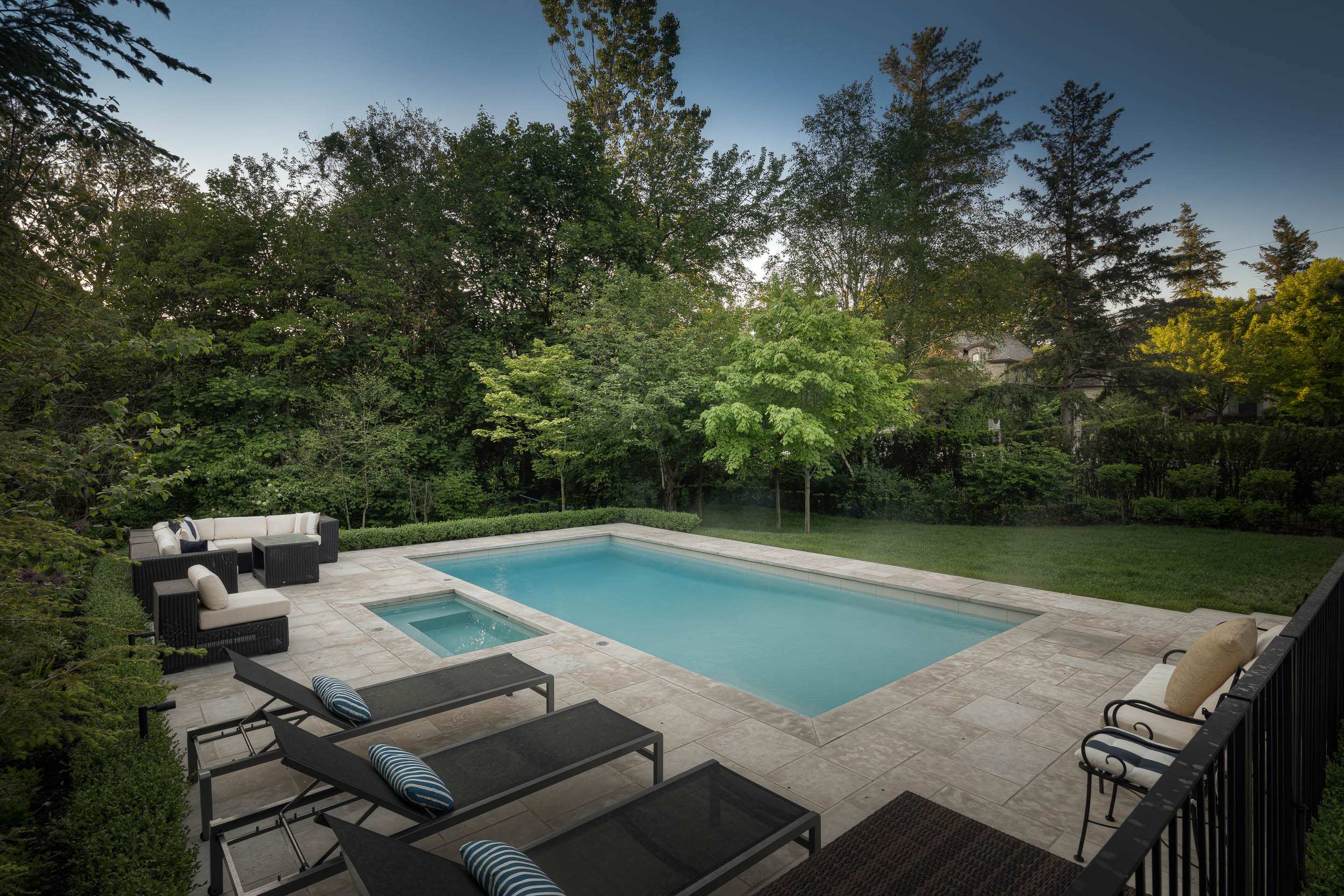 Modern backyard features a luxurious swimming pool surrounded by patio furniture and lush greenery, creating a serene outdoor living space for relaxation.