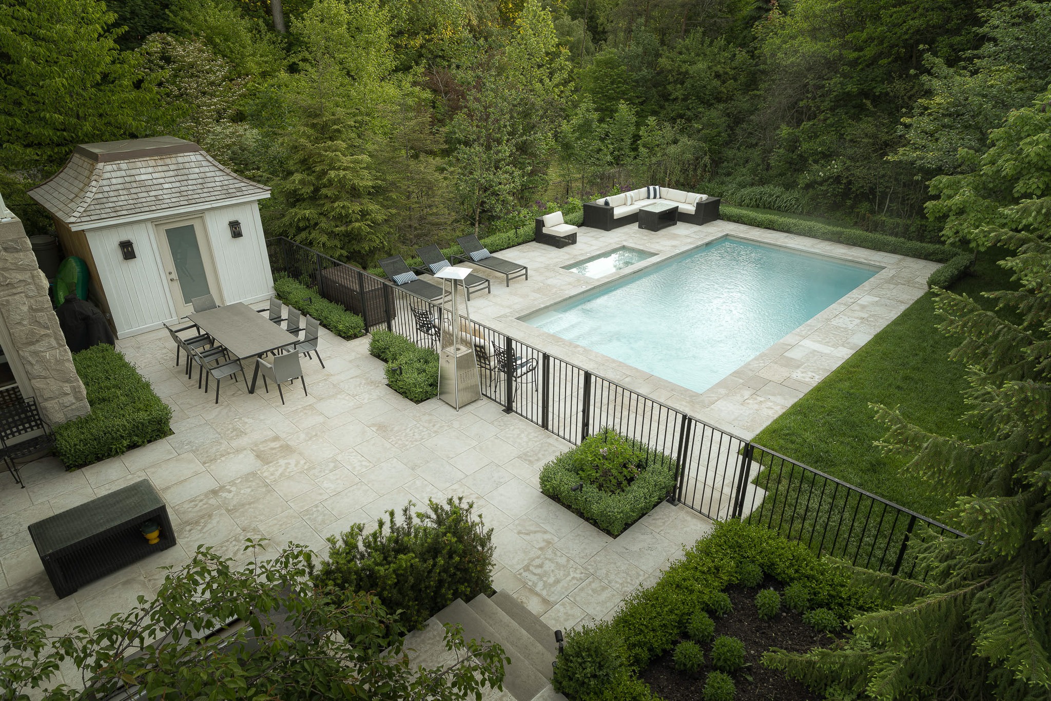 A luxurious backyard features a rectangular pool, lounge chairs, a dining table, lush greenery, and a small pavilion surrounded by a neatly manicured garden.