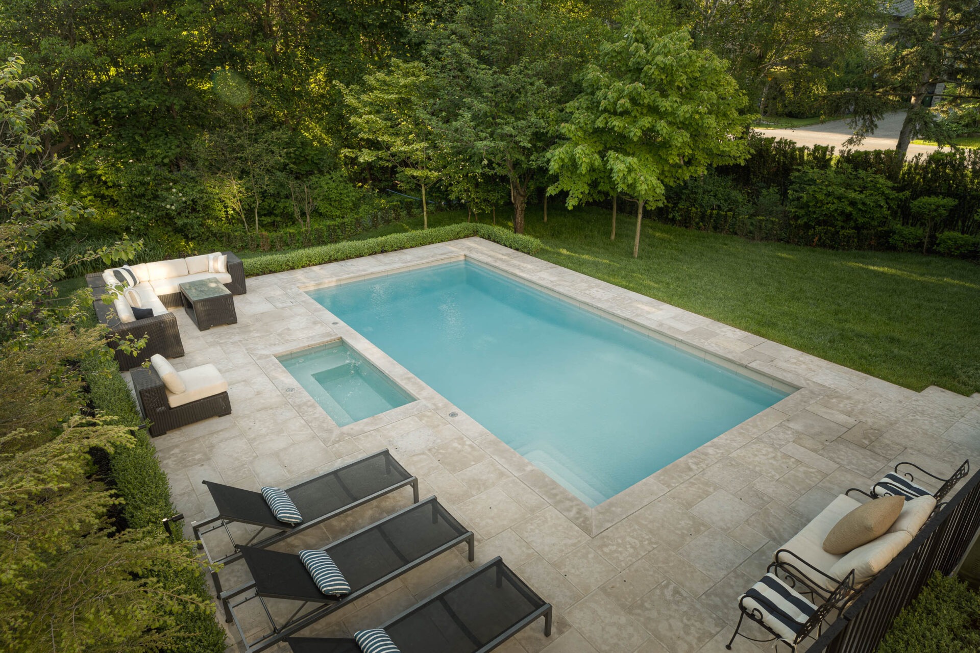 A serene backyard features a rectangular pool, lounge chairs, and patio furniture, surrounded by lush greenery and trees.