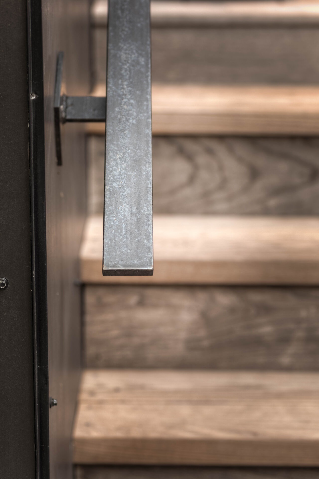 Close-up of a metal handrail alongside wooden steps, showing textures of iron and wood grain with a soft focus background.