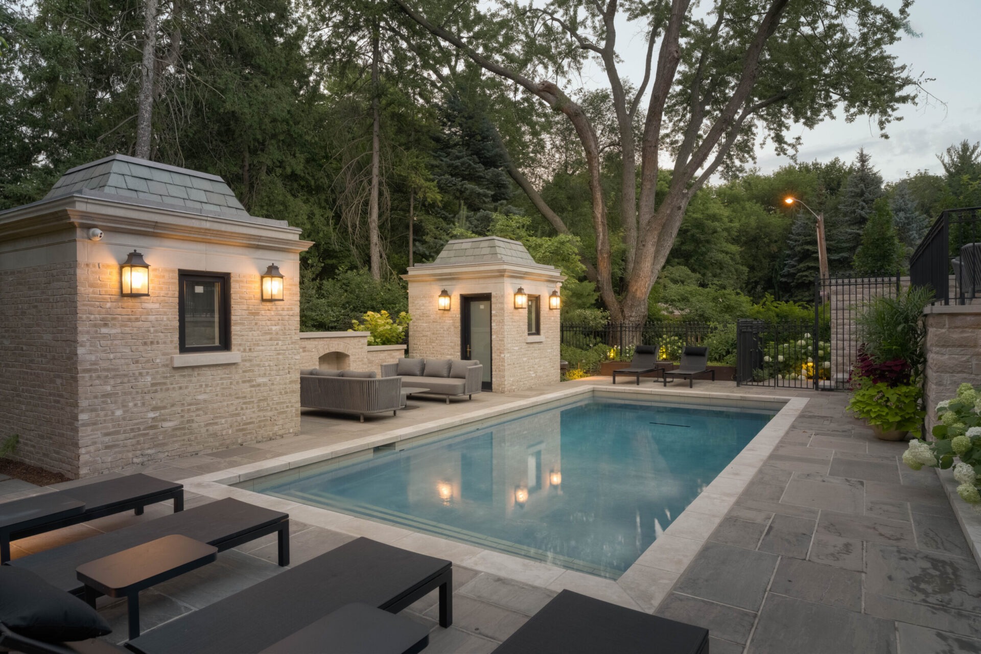 A serene backyard features a pool, lounge chairs, brick structures, and lush greenery, creating a peaceful and inviting outdoor setting.