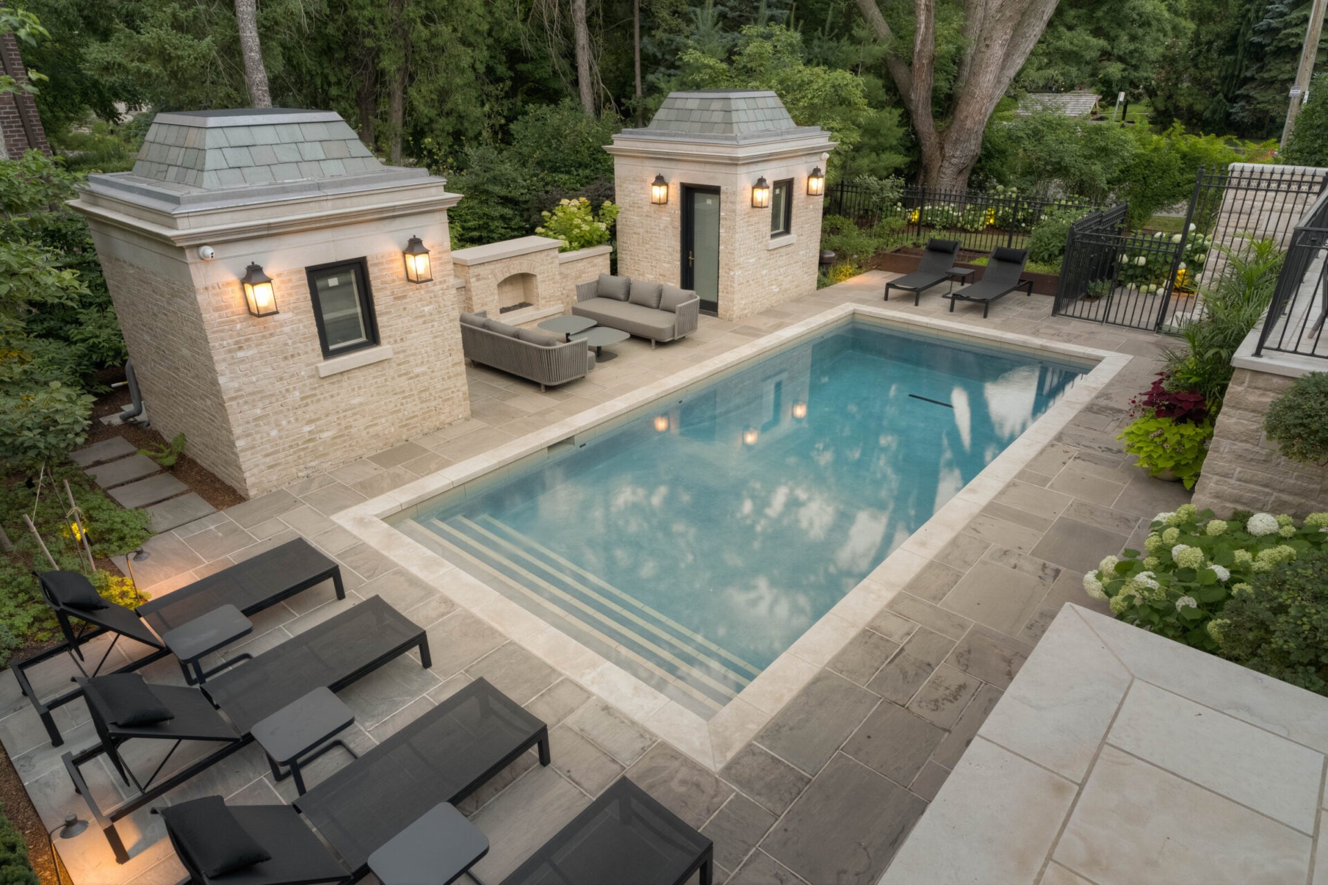 A serene outdoor pool area with elegant stone architecture, surrounded by lush greenery, featuring lounge chairs and a cozy seating arrangement.