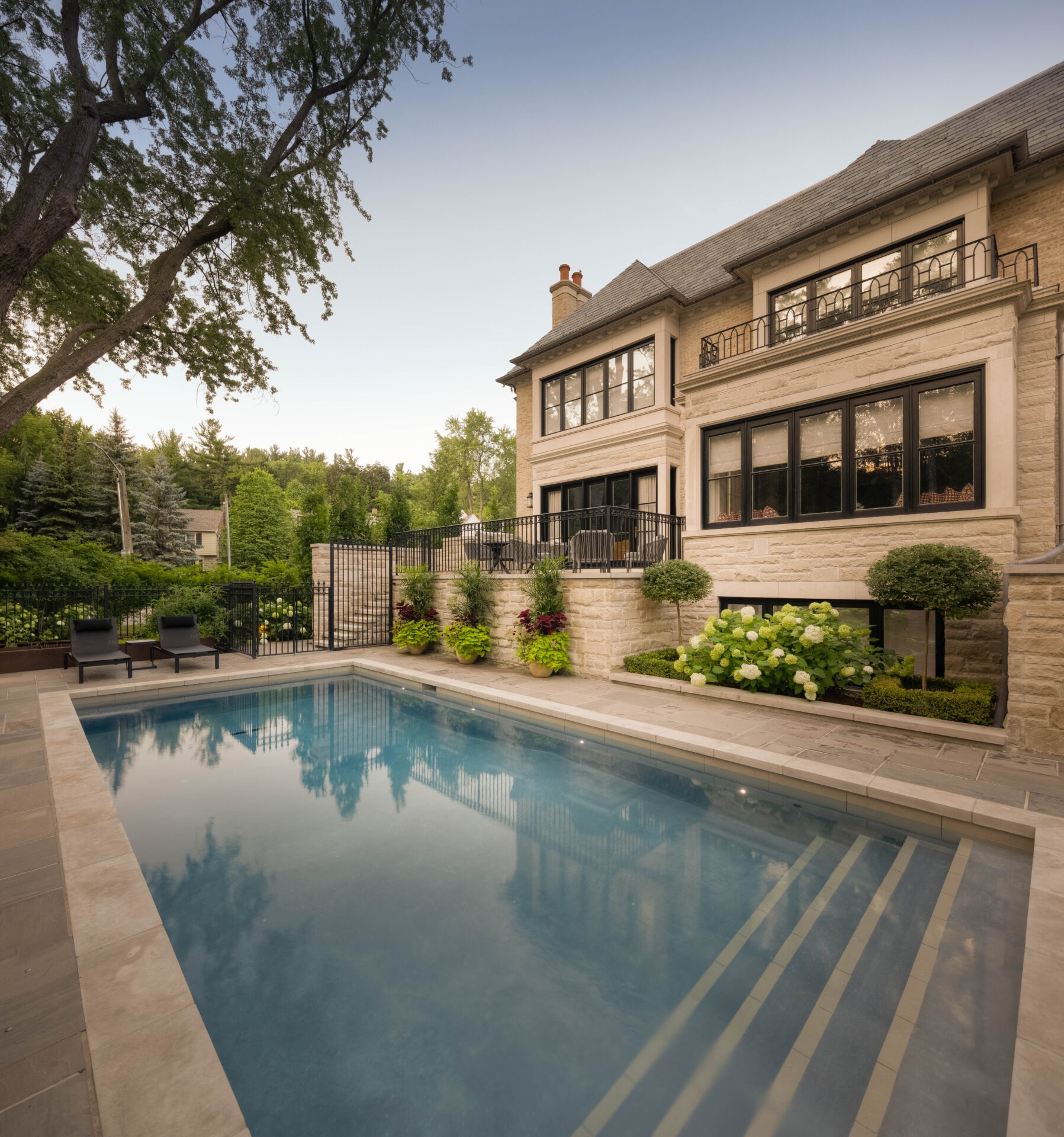 A luxurious, large house with landscaped garden and serene pool; surrounded by lush greenery and patio seating, creating an elegant outdoor space.