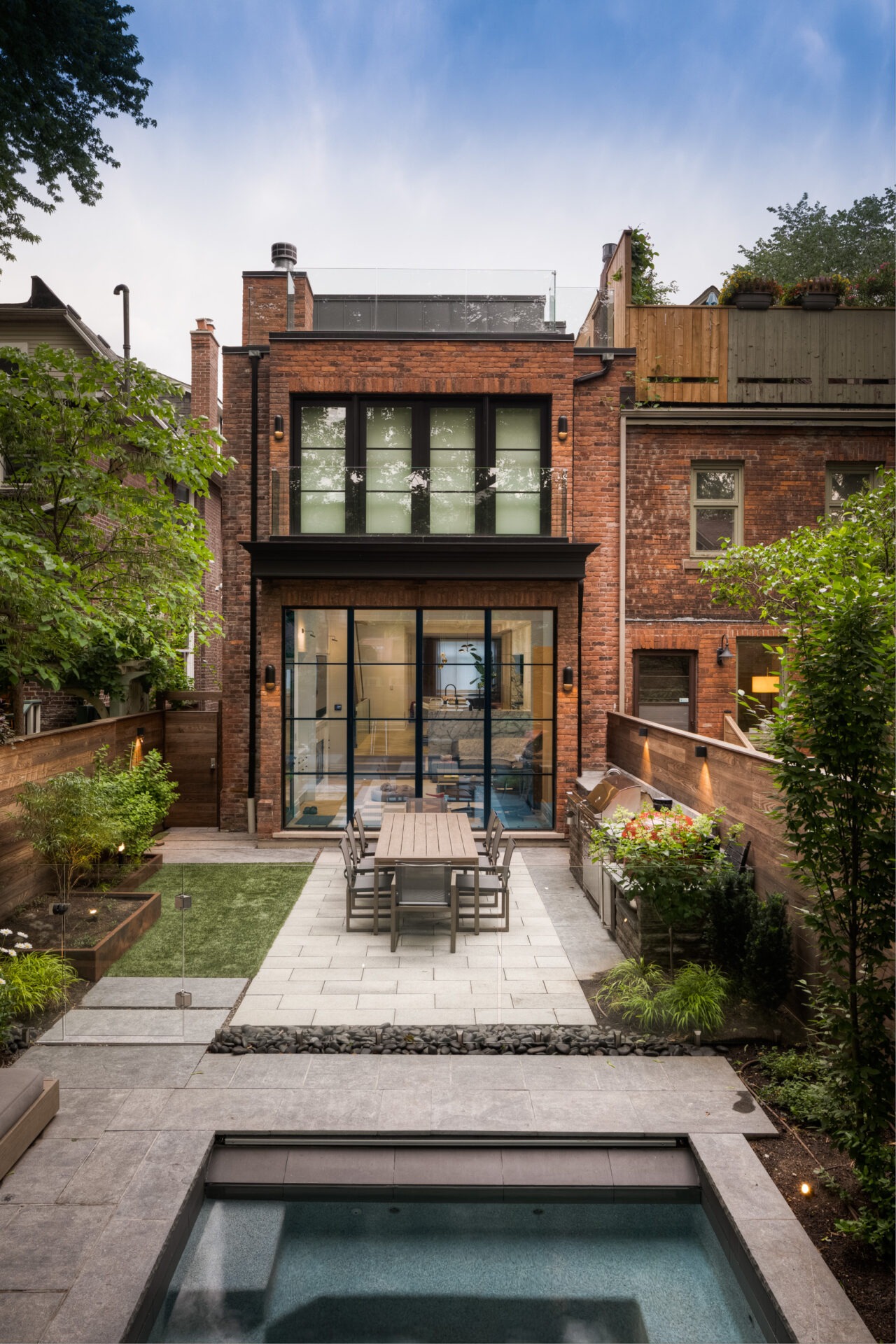 Urban backyard scene with brick house, glass doors, patio dining set, lush garden, and small pool. Modern and inviting atmosphere.