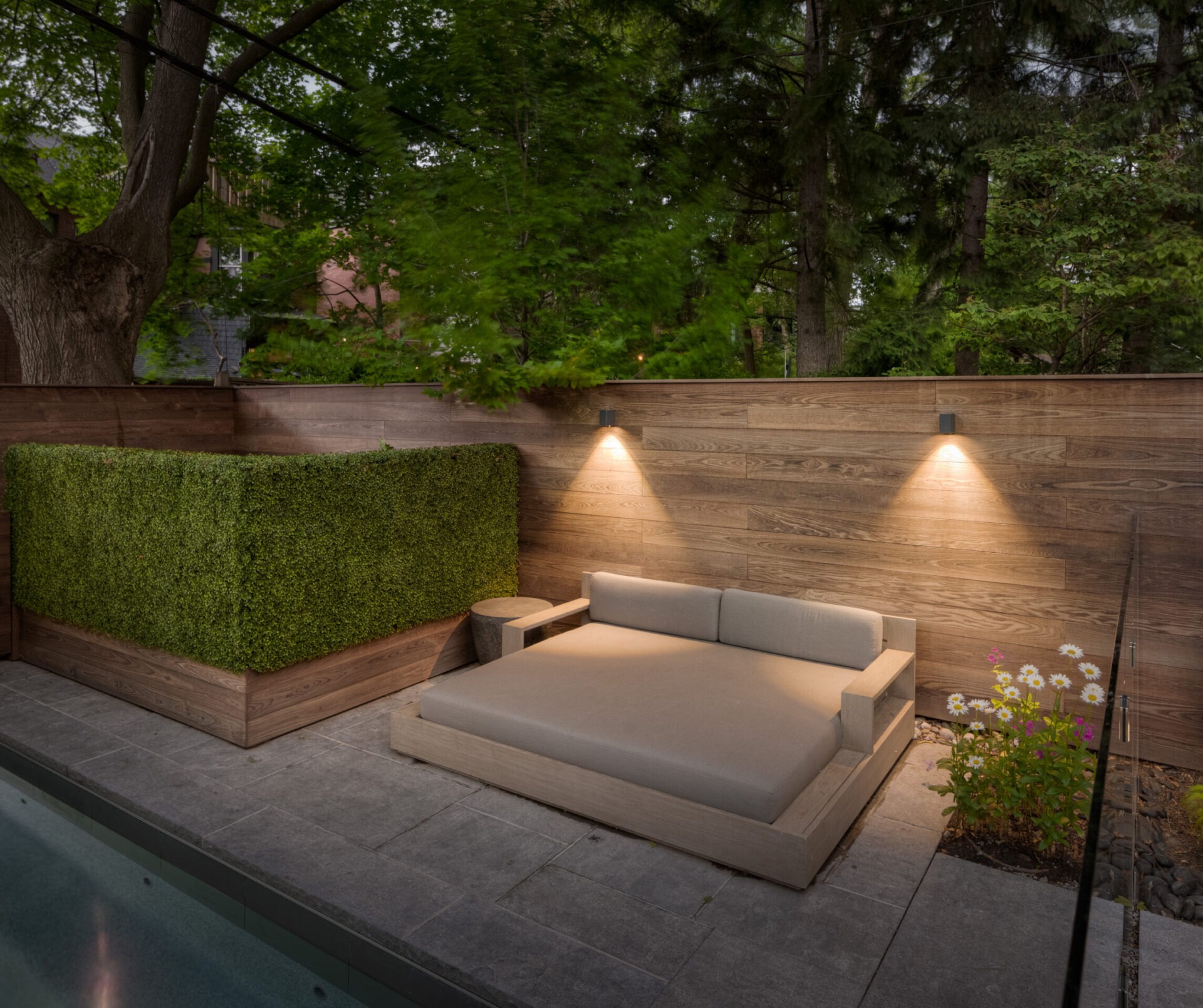 Cozy outdoor patio with modern wooden furnishings, soft lighting, lush greenery, and a serene atmosphere, perfect for relaxation and enjoying nature.