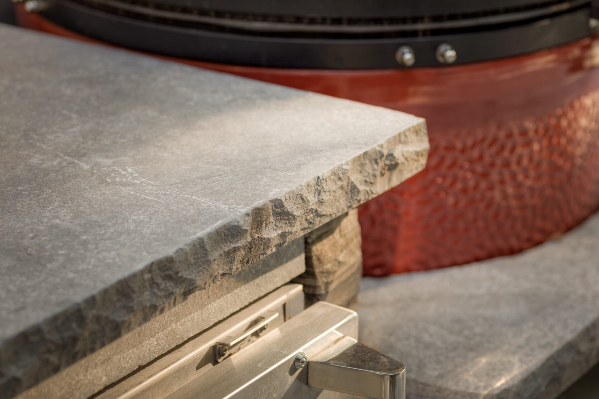 Close-up of a stone countertop with textured edges and a metallic handle, near a red and black cylindrical object.