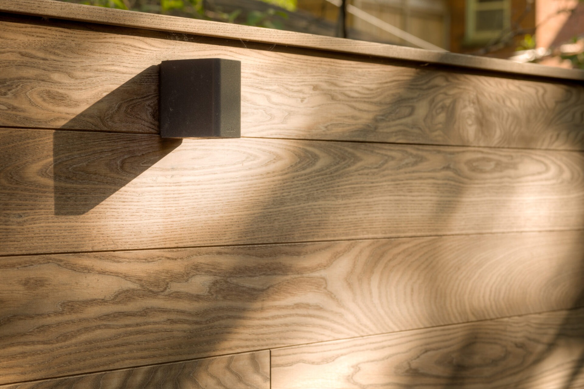 Sunlit wooden fence with prominent shadow cast by an outdoor wall light, creating an interesting play of textures and natural patterns.