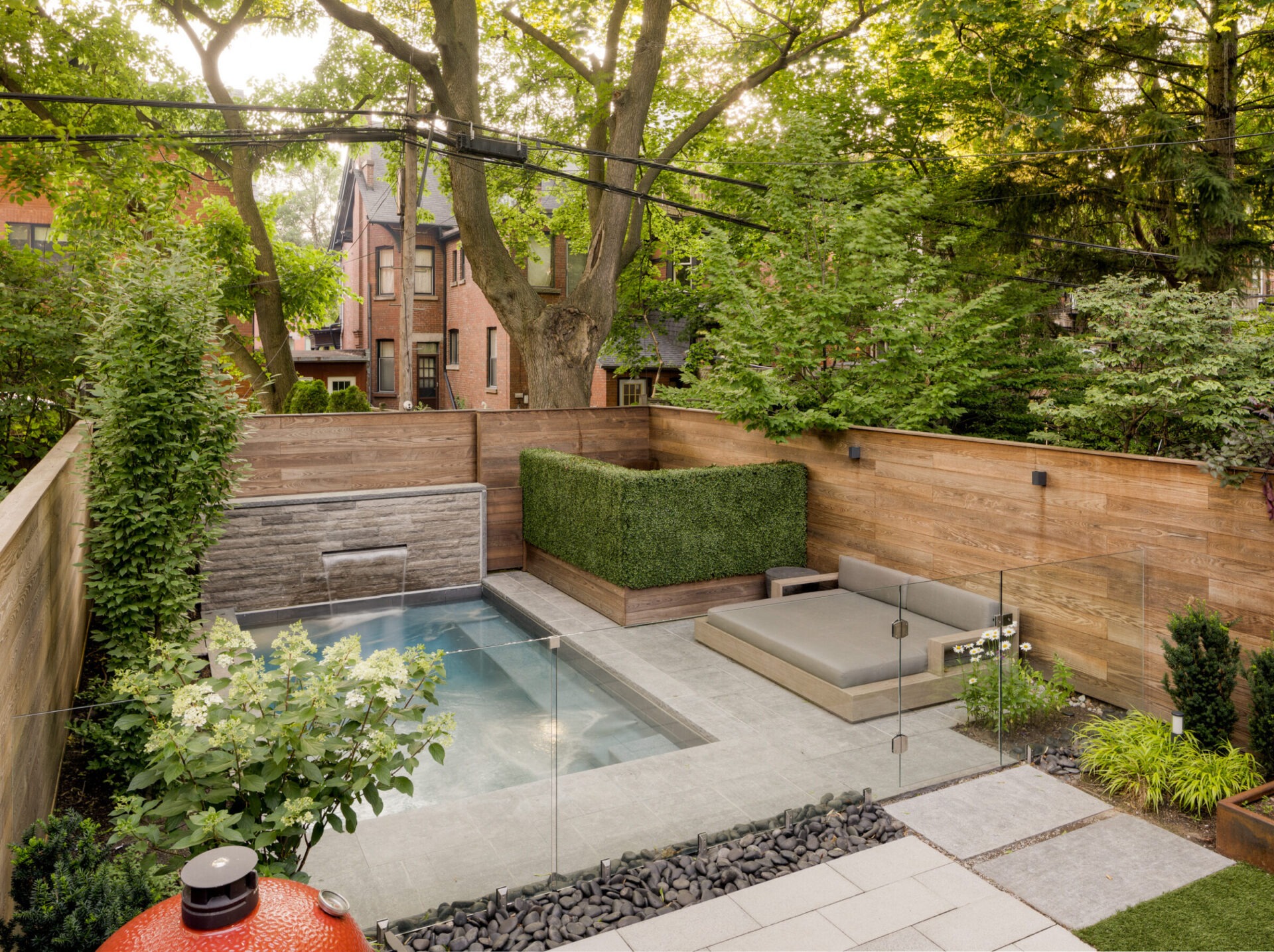 A tranquil backyard features a small pool, wooden deck, and lush landscaping. Historic brick houses are partially visible beyond the fence.