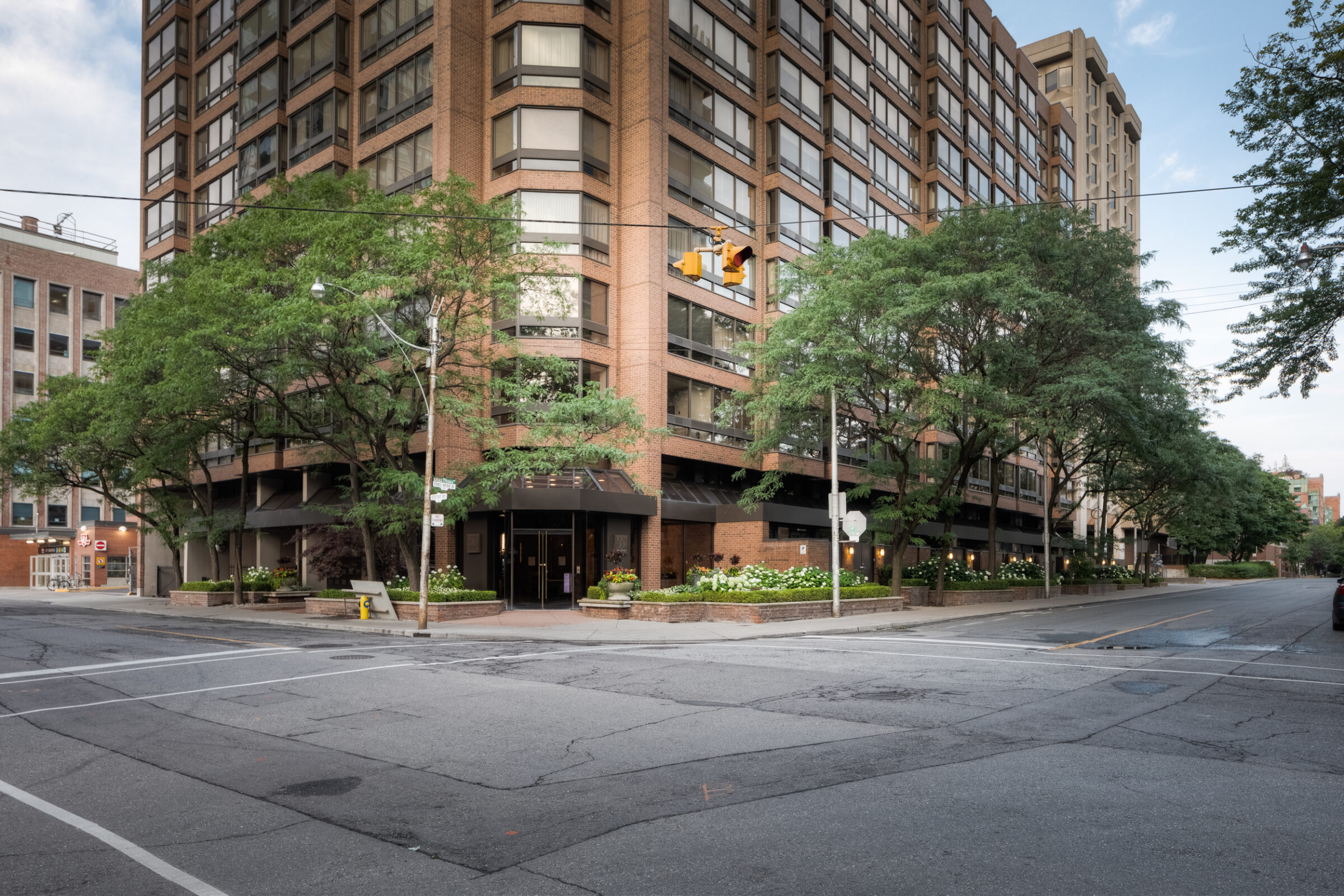 A corner building with large windows, surrounded by trees. The quiet urban setting features a few visible street signs and traffic lights.