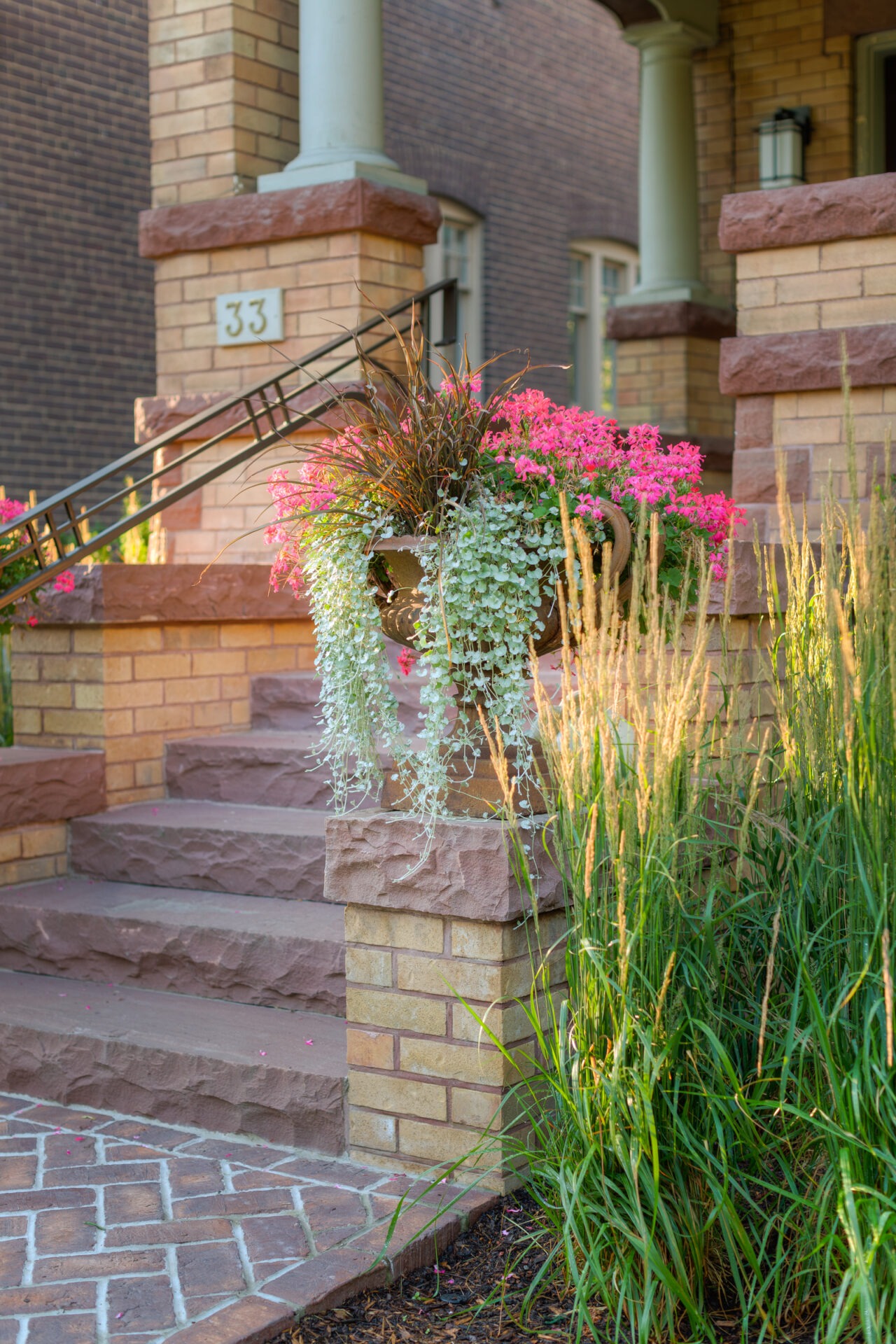 Brick steps lead to a porch with floral arrangement and greenery. The number 33 is visible. No landmarks or people present.