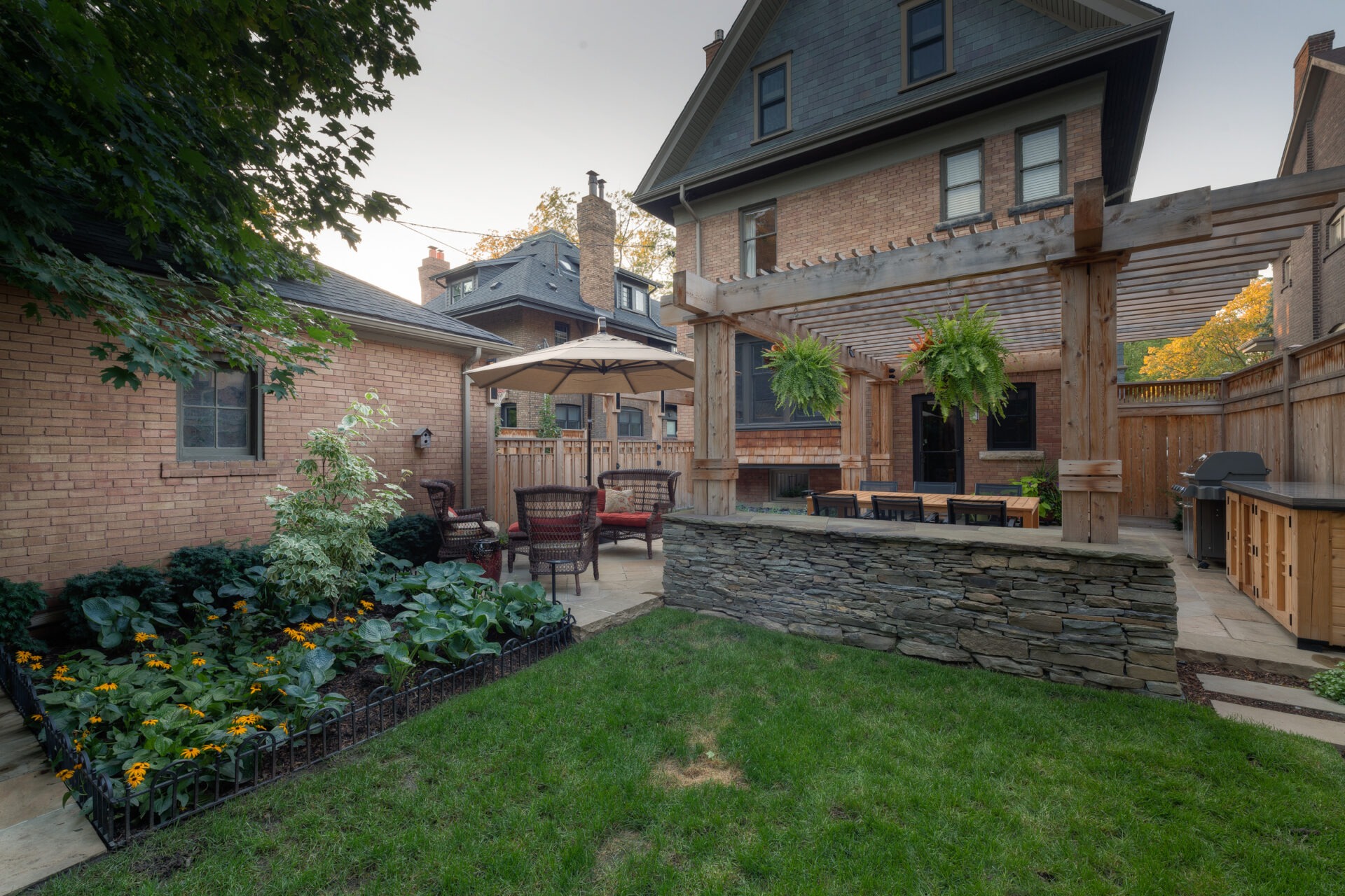 A cozy backyard with a patio, pergola, dining area, garden, and outdoor kitchen. Brick houses and greenery create a peaceful, inviting atmosphere.