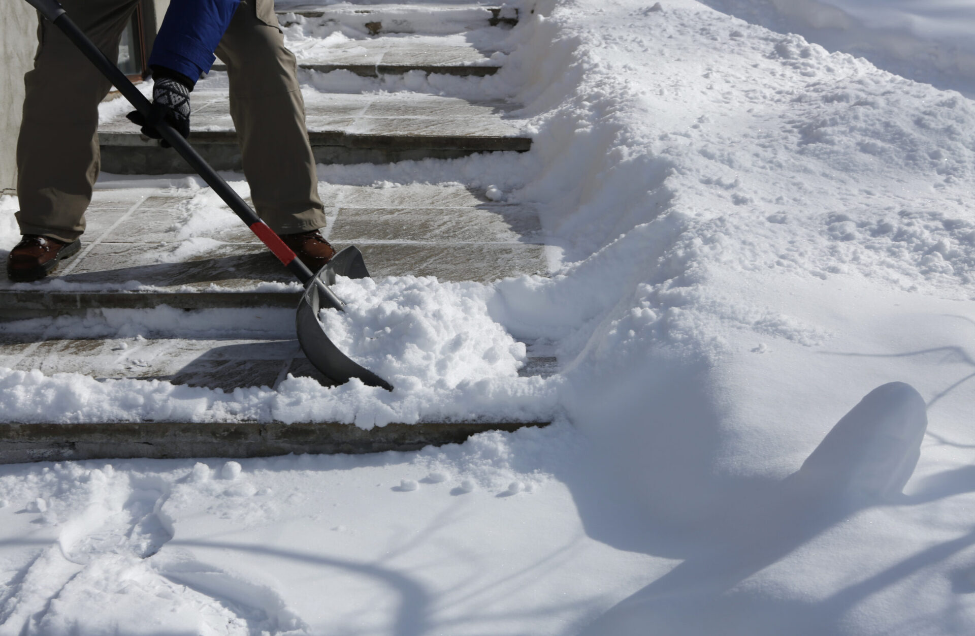 A person is shoveling snow off outdoor steps, creating a clear path surrounded by thick layers of untouched snow.