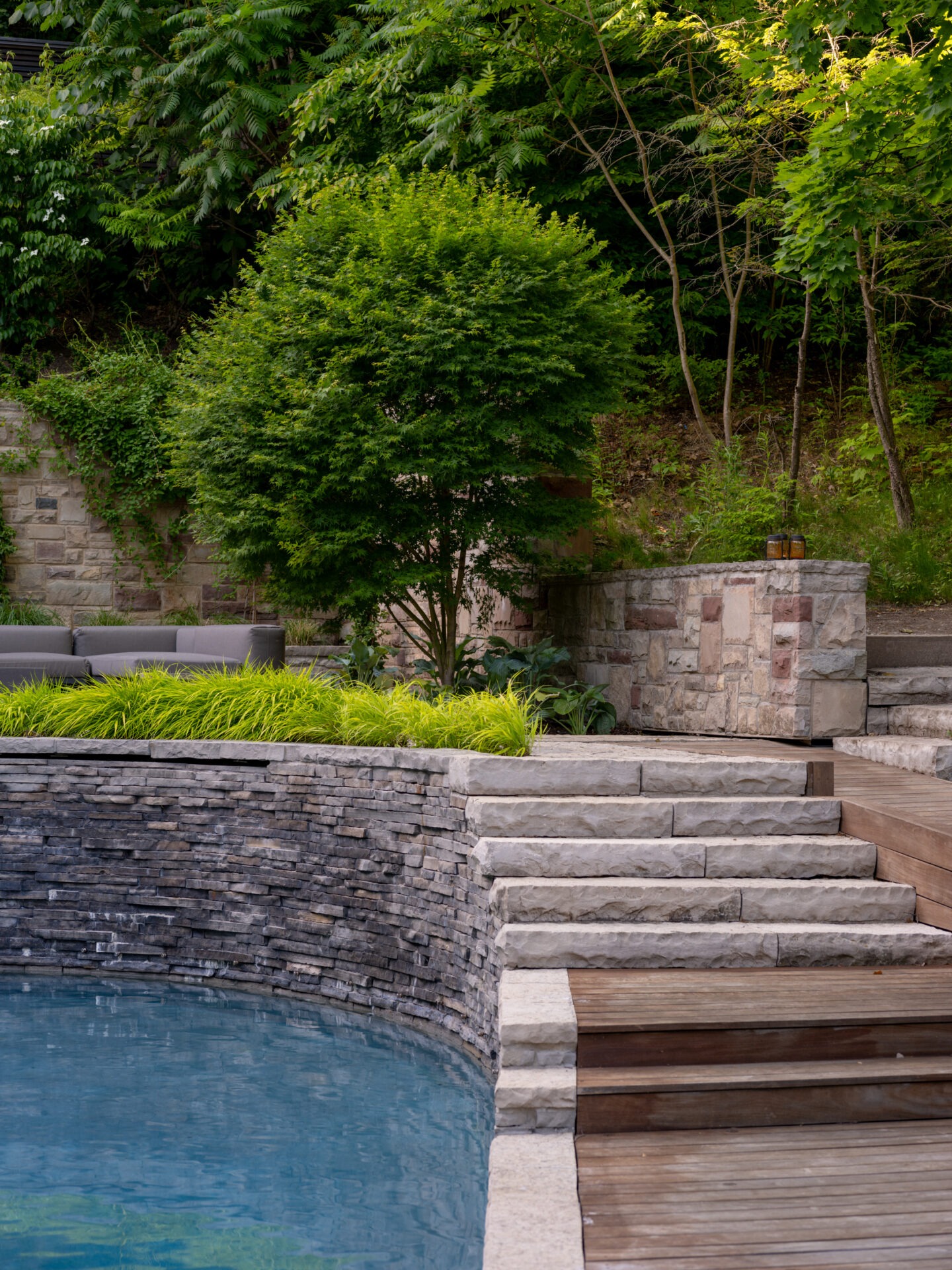 Stone steps lead to a serene outdoor pool, surrounded by lush greenery and a stone wall, creating a peaceful, natural setting.