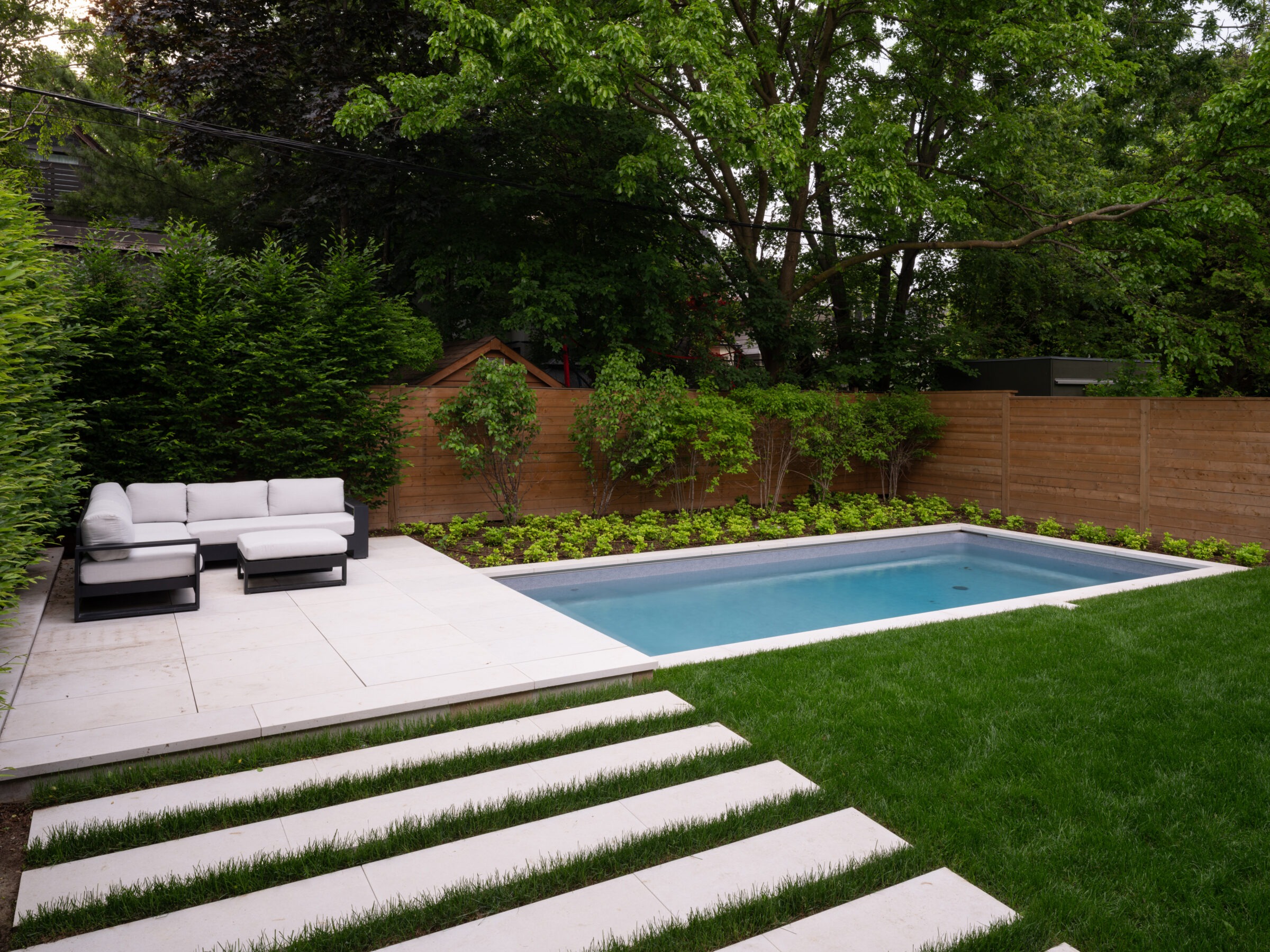 A tranquil backyard with a sleek, rectangular pool, modern outdoor seating, lush greenery, and a wooden fence creating a secluded atmosphere.