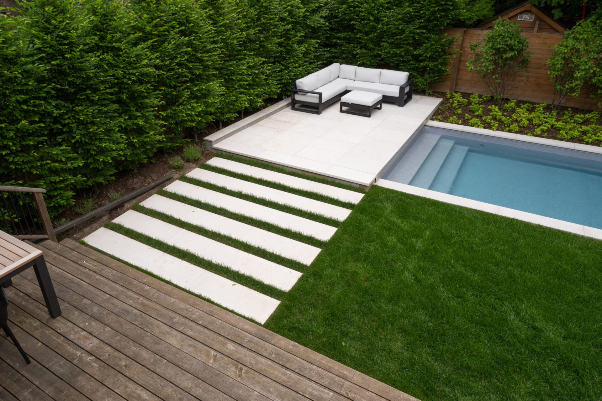 Modern backyard features a wooden deck, stylish outdoor seating area, rectangular pool, and lush greenery, creating a serene and inviting retreat.