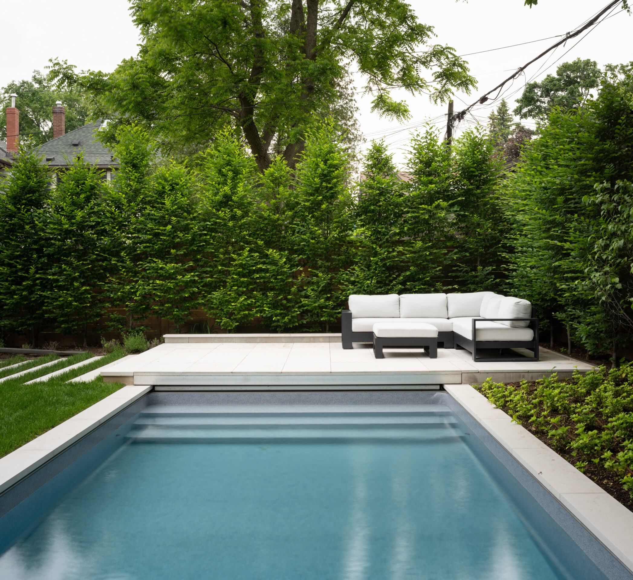 A serene backyard features a modern pool, comfortable outdoor seating, lush greenery, and a private, tranquil ambiance perfect for relaxation and leisure.
