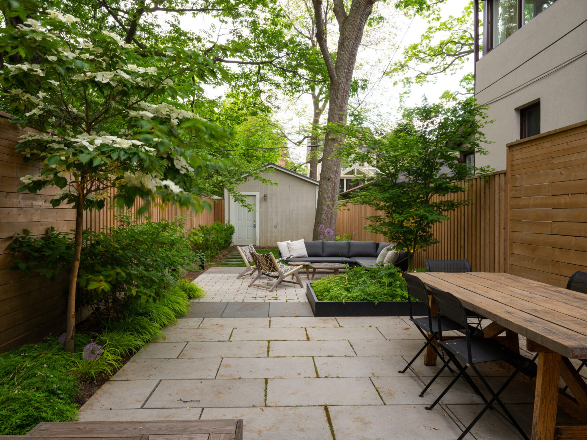 A peaceful backyard with wooden fencing, patio furniture, lush greenery, and a tree, creating a cozy and inviting outdoor space.