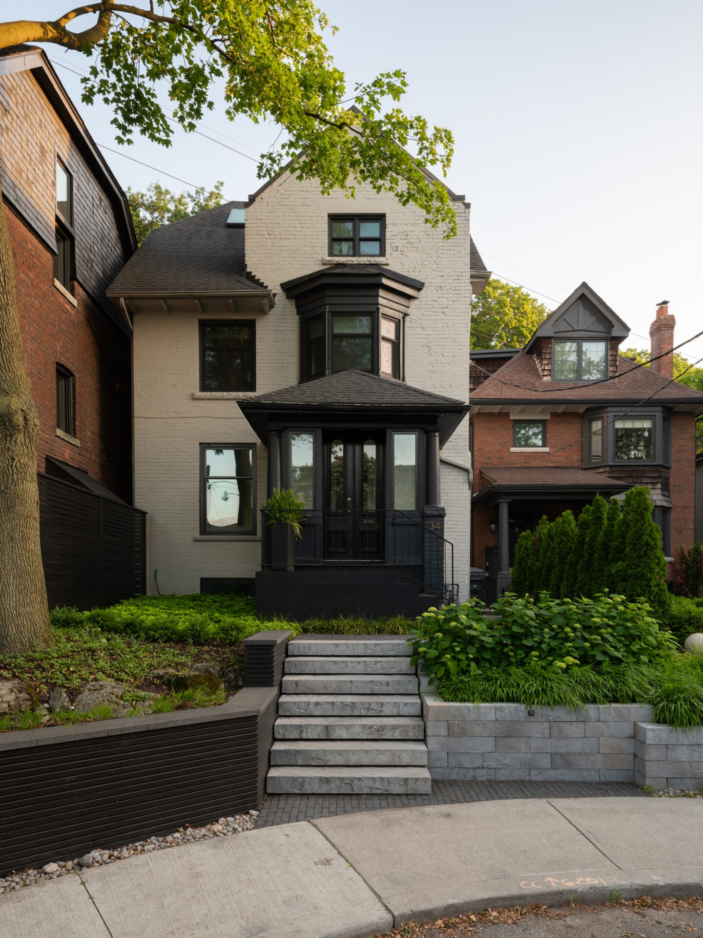 A two-story, white and brick house with a manicured garden and steps. It's nestled between similar historic-style buildings in a leafy neighborhood.