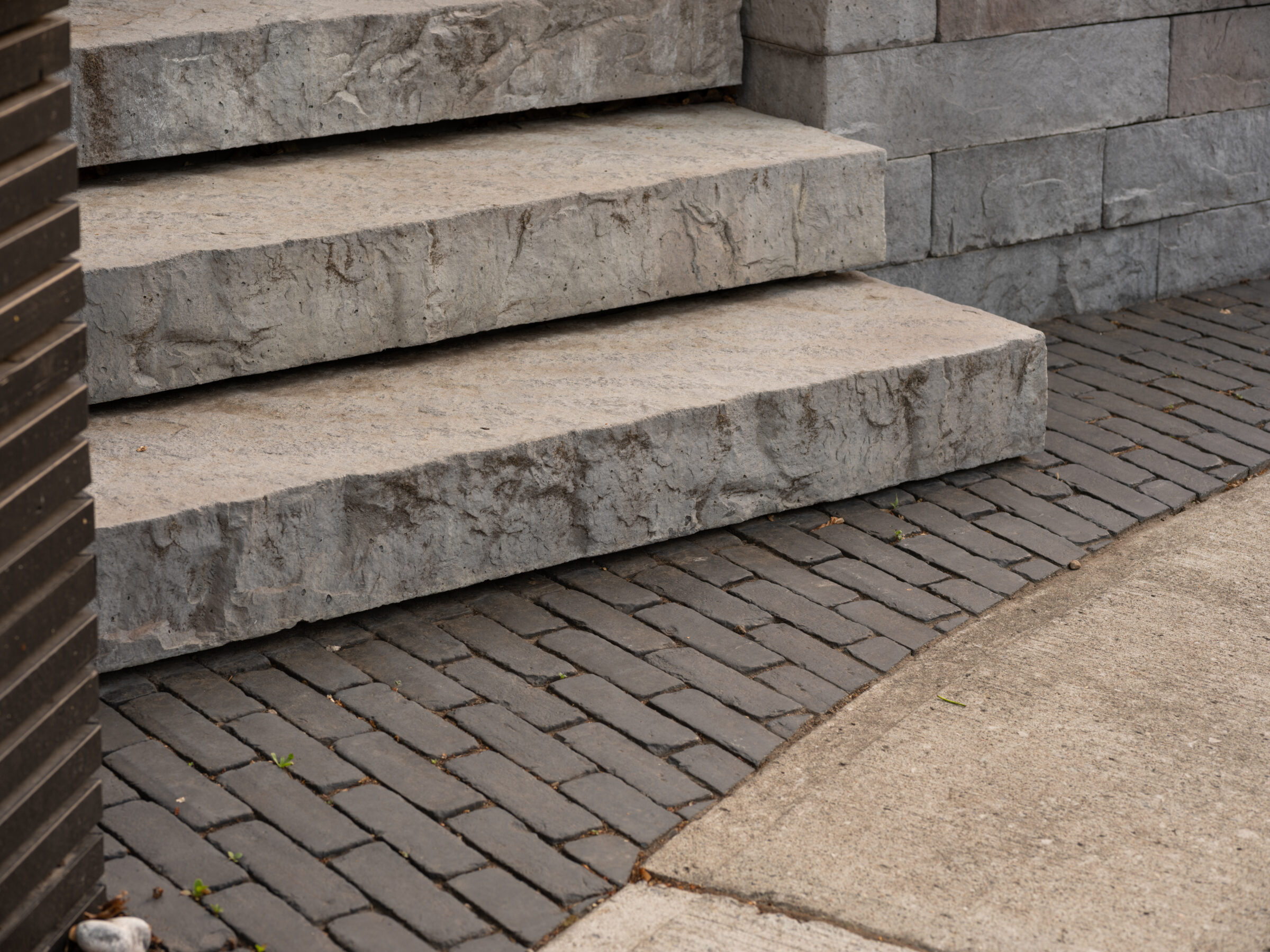 Stone steps lead to a paved path, bordered by a brick wall. Clean, minimalist design in an outdoor setting.