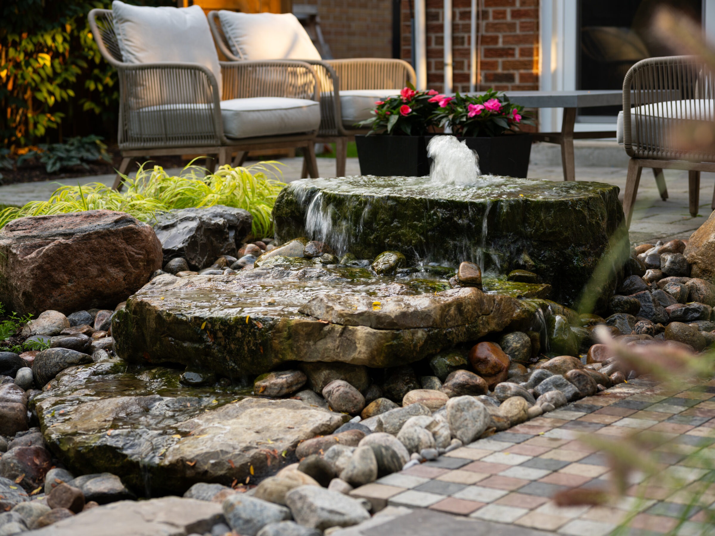 A serene backyard scene with a small stone water feature, surrounded by seating and colorful plants, creating a peaceful ambiance.