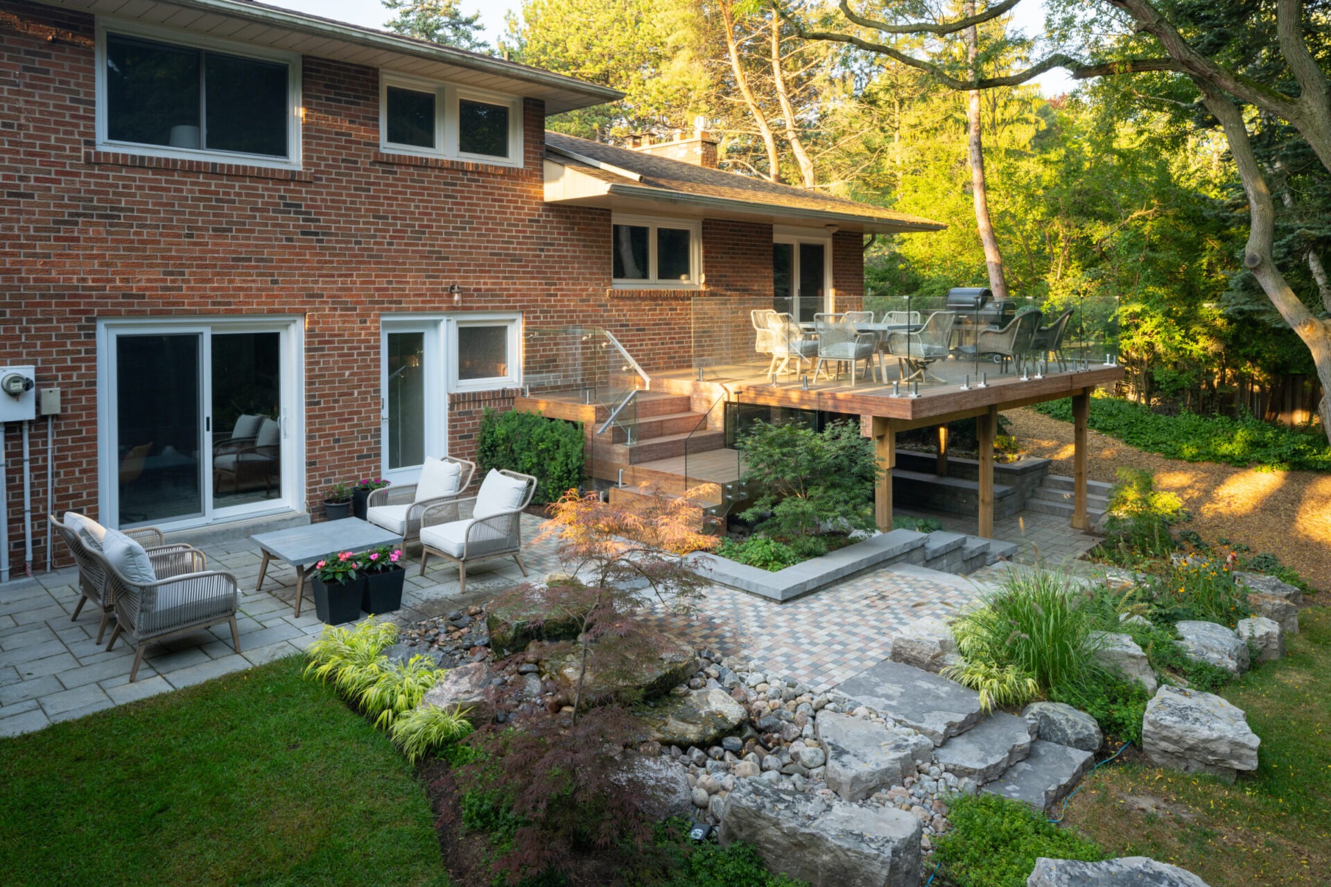 Brick house with a two-level patio, featuring outdoor seating, dining area, and landscaped garden with stone pathways and lush greenery.