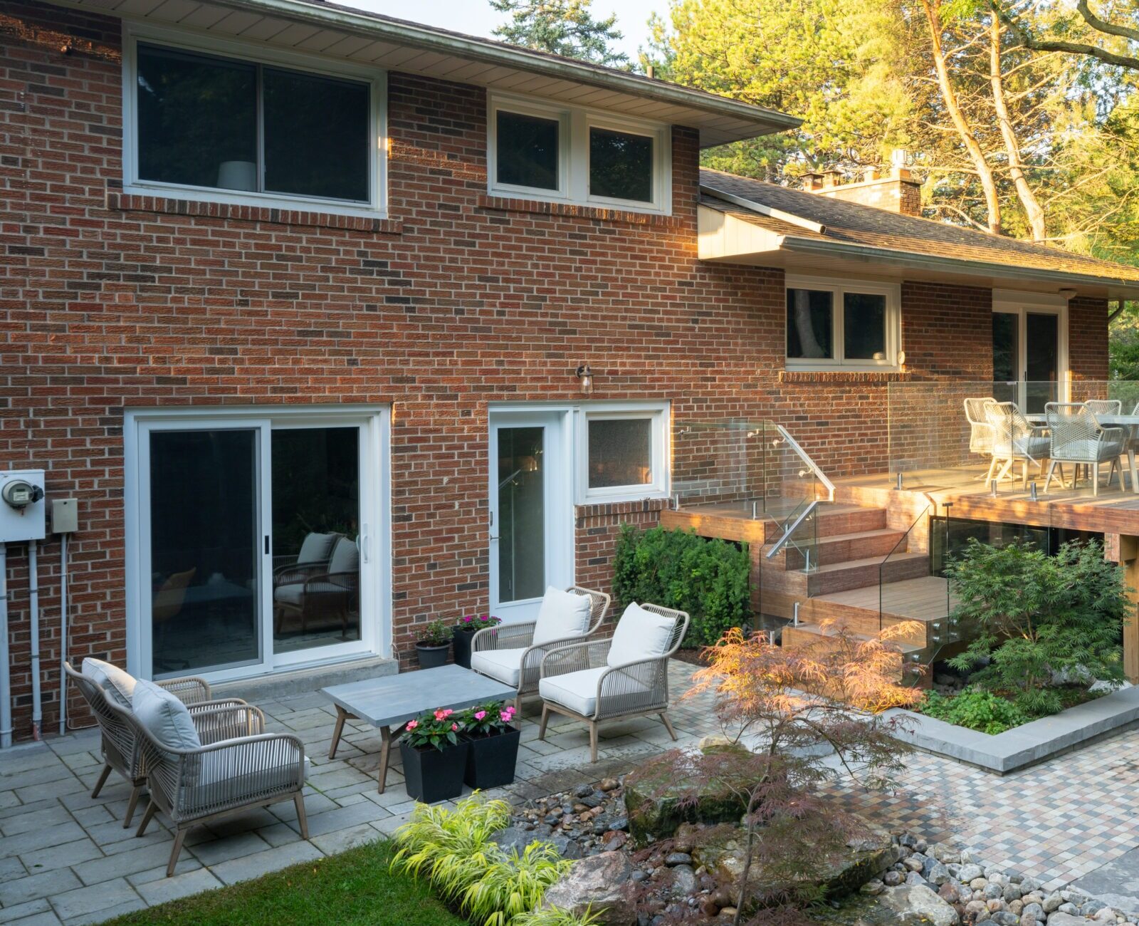 Brick house with a two-level patio, featuring outdoor seating, dining area, and landscaped garden with stone pathways and lush greenery.