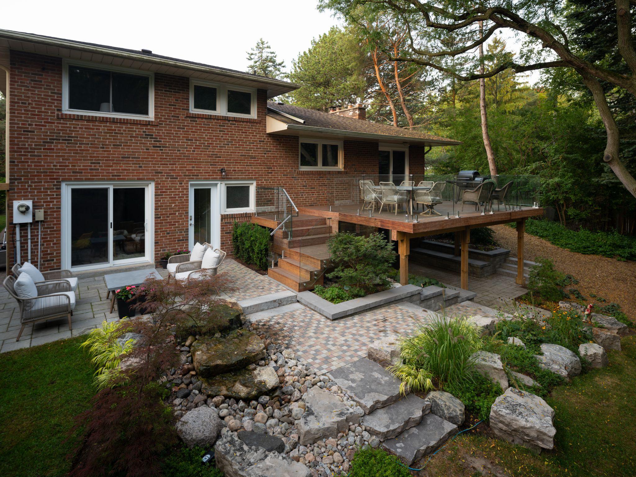 Backyard deck with glass railing, stone steps, and integrated hardscaping