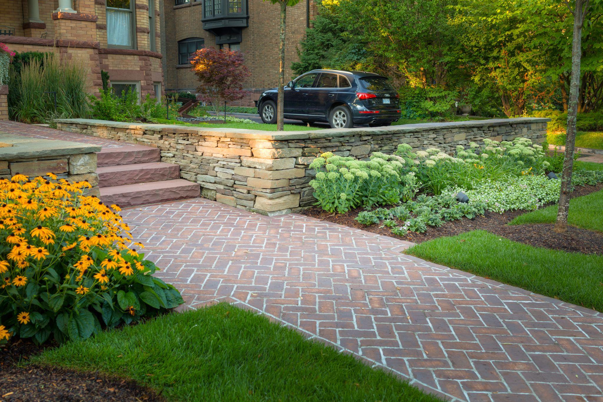 Brick walkway with natural stone retaining wall and landscaped garden beds