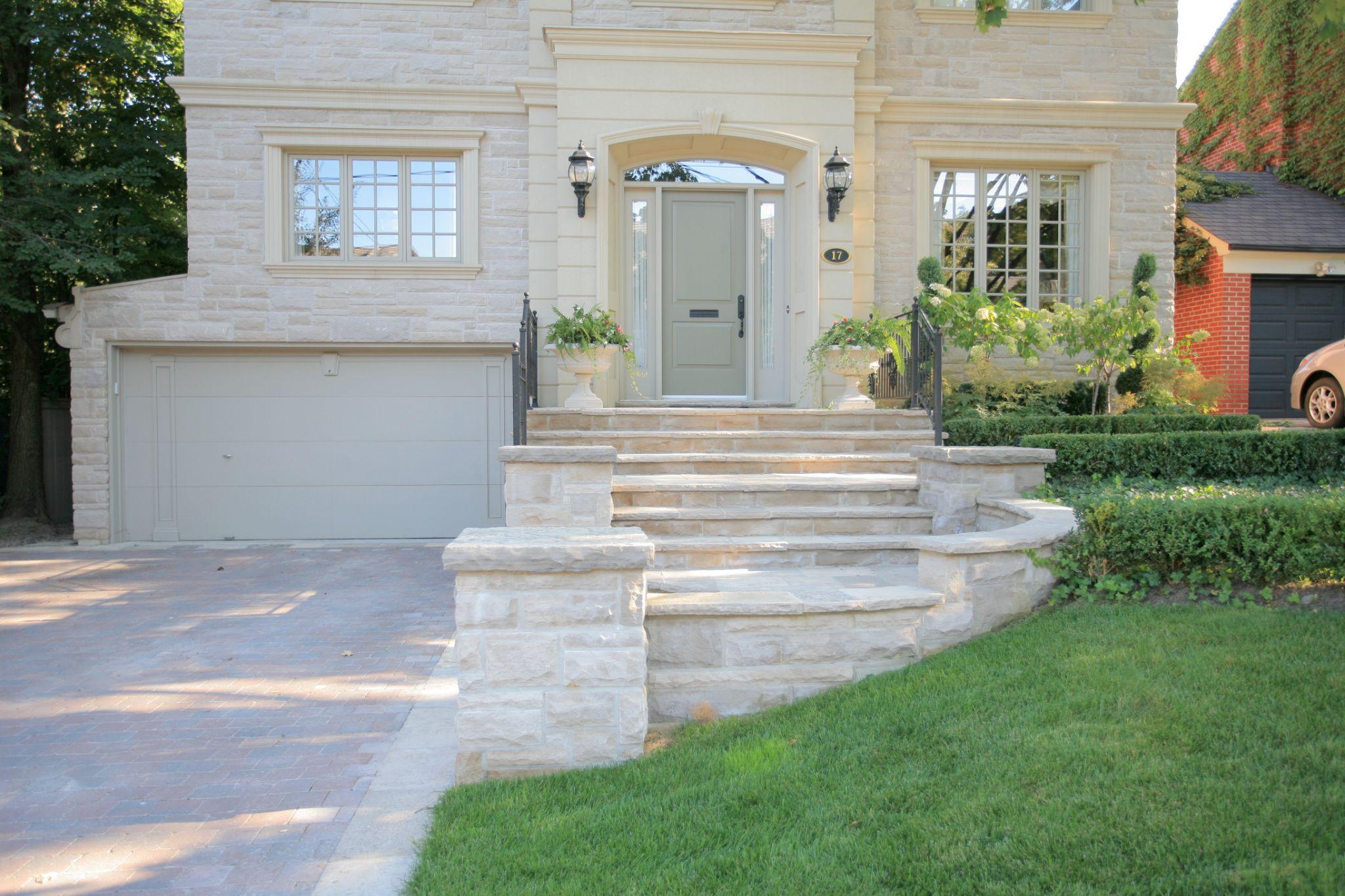 Front entrance with stone steps, paver driveway, and landscape planting